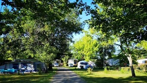 Un terrain de camping avec des emplacements pour camping-cars et des zones pour tentes, un chemin de gravier et des arbres.