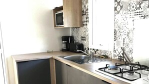 A compact kitchen with a built-in microwave, a gas stove, and a coffee maker. - ZEcamping 4 étoiles piscine couverte animations jacuzzi locatif TV 28m2 (Aureilhan)