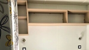A bedroom with a bed, a headboard, a shelf above the bed, and a wall-mounted light fixture. - ZEcamping 4 étoiles piscine couverte animations jacuzzi locatif TV 28m2 (Aureilhan)
