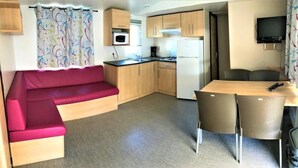 A compact living space with a kitchenette, a sofa, a dining table with chairs, and a television. - ZEcamping 4 étoiles animé piscine couverte dog friendly jacuzzi locatif TV (Aureilhan)