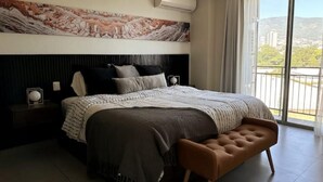 Een moderne slaapkamer met een groot bed, een bankje, een nachtkastje en uitzicht op de omgeving.