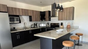 Een moderne keuken met donkere kastjes, een centraal kookeiland met krukken, een magnetron, fornuis en diverse apparaten.