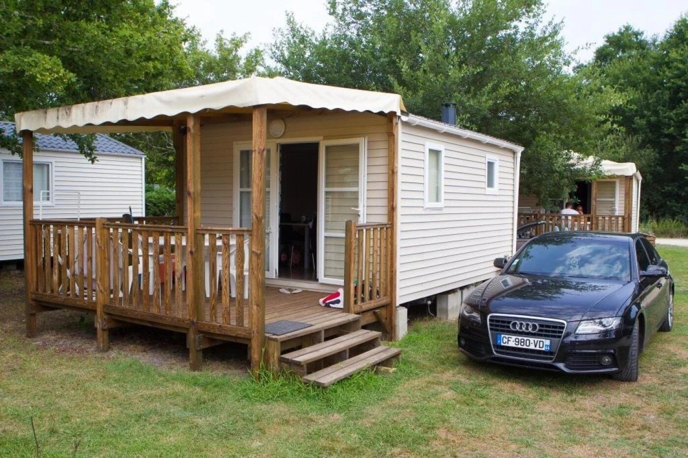 Une maison mobile dotée d’une terrasse en bois et d’une voiture garée devant.