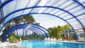 Una piscina techada con techo azul, rodeada de sillas de descanso y una terraza de madera.