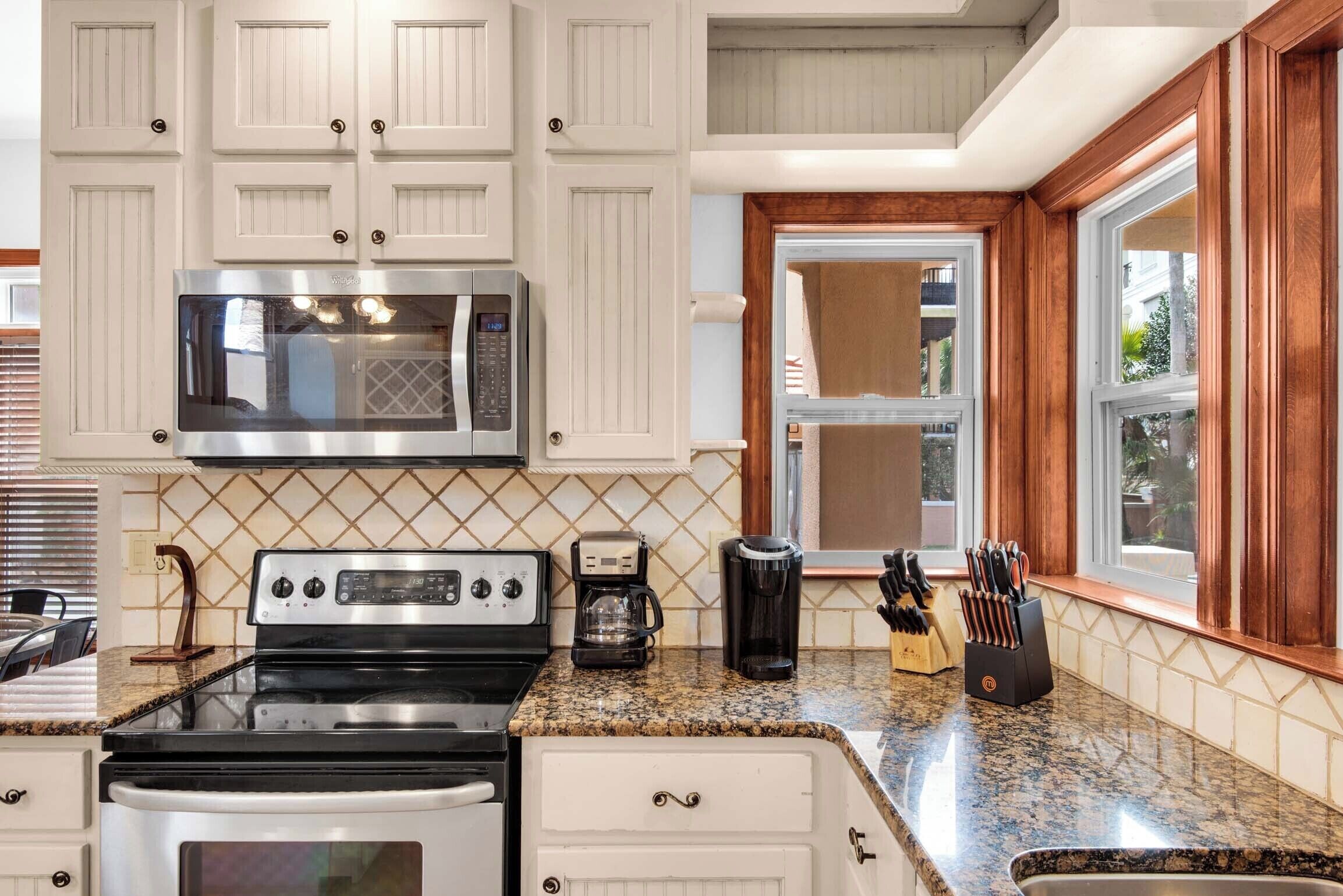 A kitchen with white cabinets, a stainless steel microwave, a stove, and a coffee maker.