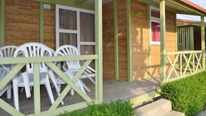 Un edificio de madera con un porche cubierto, sillas de plástico blancas y un letrero que dice 'CAMPING'.