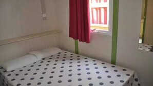 Una habitación pequeña con cama individual, colcha de lunares, ventana con cortina roja y detalles verdes en las paredes.