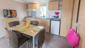 Une cuisine compacte avec un coin repas, un téléviseur et un sac rose accroché au mur.