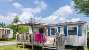 Une maison mobile dotée d’un porche, d’une petite terrasse et d’une fenêtre avec des volets bleus.