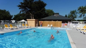 Une piscine avec des personnes dedans, entourée de chaises longues et délimitée par une clôture.
