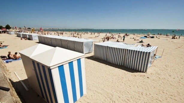 A beach with striped beach huts and a sandy shore.