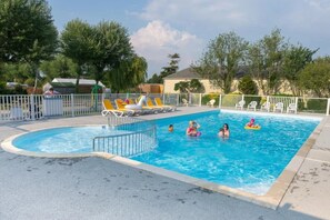 A swimming pool with a fenced area, lounge chairs, and a clear sky.