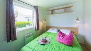 A room with a bed, a window with curtains, a radiator, and a shelf above the bed. - ZEcamping 3 étoiles animaux acceptés avec piscine chauffée à Guérande (Guérande)