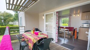 A covered patio with a table set for dining, chairs, and a pink blanket. - ZEcamping 3 étoiles animaux acceptés avec piscine chauffée à Guérande (Guérande)