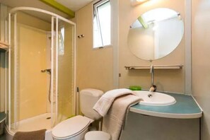 Een badkamer met douche, toilet, wastafel en spiegel.