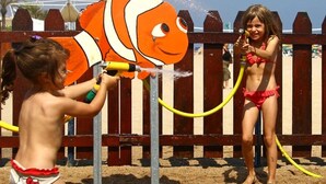 Two children playing with a water fountain shaped like a clownfish.