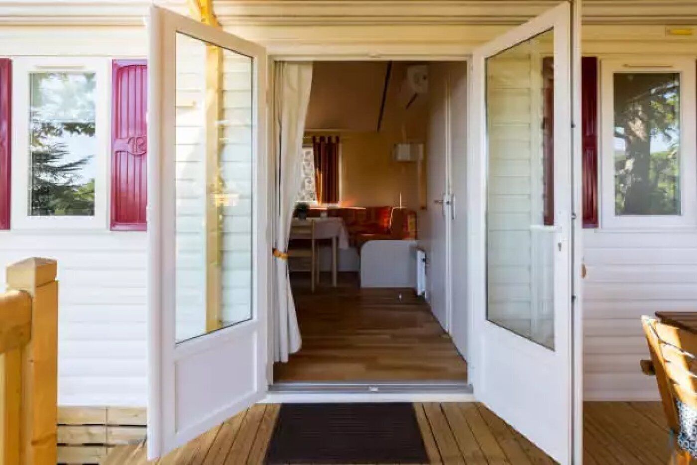 A wooden deck leading to a white cabin with a kitchen area visible through an open door.