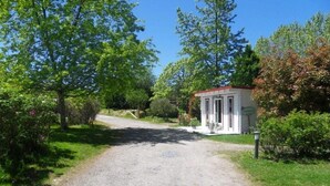 A gravel driveway leading to a white building with a red roof, surrounded by lush greenery and trees. - ZEcamping 3 étoiles piscine mobil-home TV 29m2 5 pers (Urt)