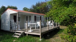 Ein kleines, eingeschossiges Mobilheim mit Veranda und Sitzbereich im Freien.
