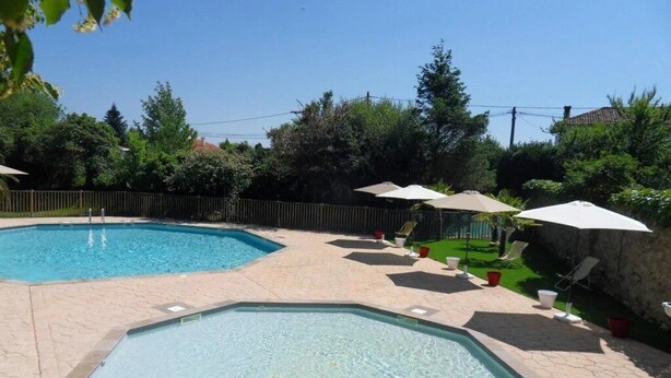 Ein Poolbereich mit zwei Pools, umgeben von einer gepflasterten Terrasse und Sonnenschirmen.