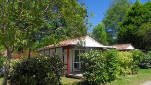 A small house with a tiled roof, surrounded by lush greenery and trees. - ZEcamping 3 étoiles piscine pet friendly bien-être locatif TV 22m2 4 pers (Urt)