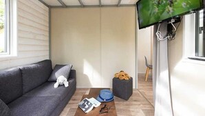 A cozy living room with a grey sofa, a small table with a book and glasses, a blue hat, and a teddy bear. - ZEcamping 4 étoiles espace aquatique chalet TV BBQ clim 35m2 (Loupiac)
