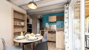 A compact kitchen with a dining area, wooden cabinets, and a large window. - ZEcamping 4 étoiles espace aquatique chalet TV BBQ clim 35m2 (Loupiac)