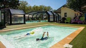 Ein Schwimmbecken mit zwei Schwimmern, umgeben von einer überdachten Liegefläche mit Stühlen und einem Gebäude.