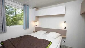 Ein Schlafzimmer mit einem Bett, einem Fenster mit Vorhängen und einem an der Wand befestigten Regal.