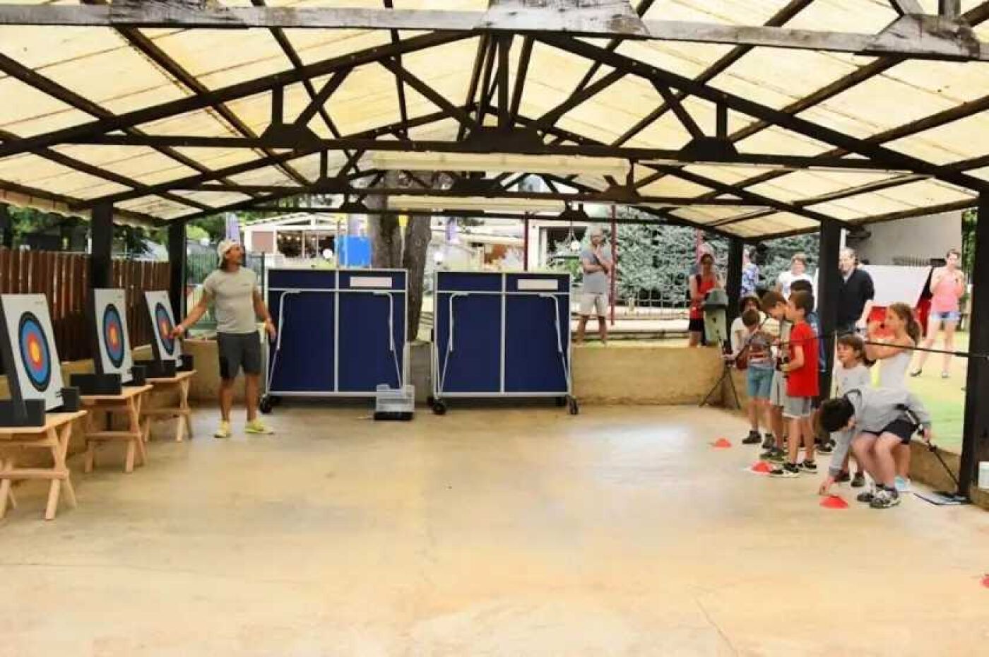 An indoor archery range with targets, a covered area, and a group of people.