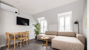 A modern living room with a sectional sofa, a dining table with chairs, a small side table, a potted plant, and a flat-screen TV mounted on the wall. - One Bedroom Apartment, Sleeps 2 (London)