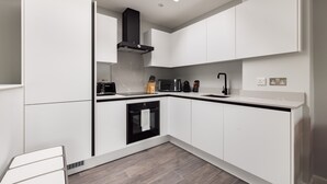 A modern kitchen with white cabinetry, a black range hood, a microwave, a toaster, and a sink. - One Bedroom Apartment, Sleeps 2 (London)