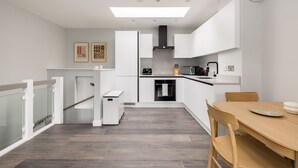 A modern kitchen with white cabinetry, a built-in oven, and a dining area with a wooden table and chairs. - One Bedroom Apartment, Sleeps 2 (London)
