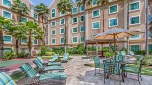 A hotel courtyard with lounge chairs, a covered seating area, and palm trees. - Suites at Lake Buena Vista close Disney Spring (Orlando)