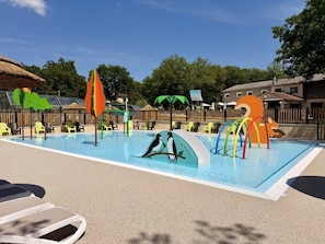 Ein Schwimmbad mit Rutschen, Liegestühlen und einem Spielbereich mit bunten Bauwerken.