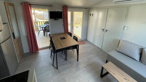 A compact room with a dining table, a sofa, and a TV mounted on the wall. - ZEcamping 3 étoiles familial piscine couverte locatif TV LV BBQ 33m2 (Les Moutiers-en-Retz)
