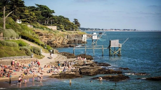 Una playa costera con afloramientos rocosos, un muelle de madera y una vista despejada del mar.