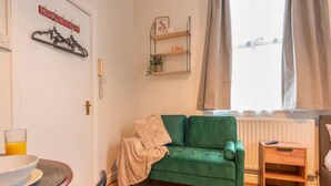 Uma sala de estar acolhedora com um sofá verde, uma pequena mesa lateral de madeira, um radiador e uma janela com cortinas.