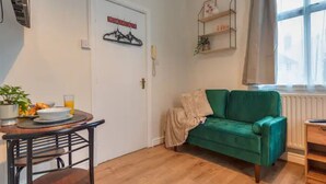 Uma sala de estar acolhedora com um sofá verde, uma mesa de centro de madeira com itens de café da manhã, um porta-roupas suspenso e uma janela com vista.
