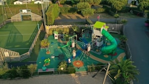 Une aire de jeux avec des toboggans et des structures d’escalade, entourée d’une clôture et de verdure.