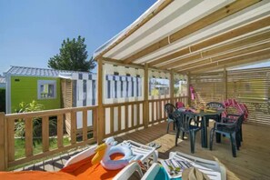 A covered outdoor area with a wooden deck, a table with chairs, and a pool with inflatable toys.