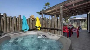 A hot tub with a wooden deck, a covered patio area, and a fenced backyard.
