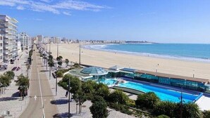 A coastal hotel with a pool, beachfront view, and a road running parallel to the beach.