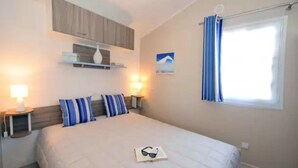 A bedroom with a bed, two bedside lamps, a nightstand, a window with curtains, and a wall-mounted shelf with a vase.