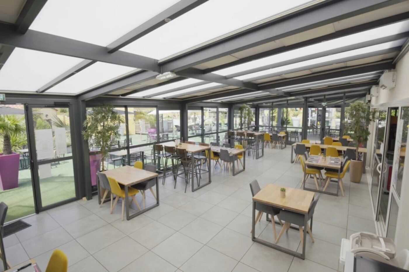 Un espace intérieur spacieux, aménagé avec des tables et des chaises, de grandes fenêtres et un plafond avec des poutres apparentes.