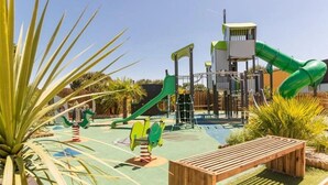 Une aire de jeux avec un toboggan, des structures d’escalade et un banc en bois.