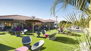 Un espace extérieur aménagé avec des chaises et des tables modernes, un bâtiment doté d’un toit en tuiles et un ciel dégagé.