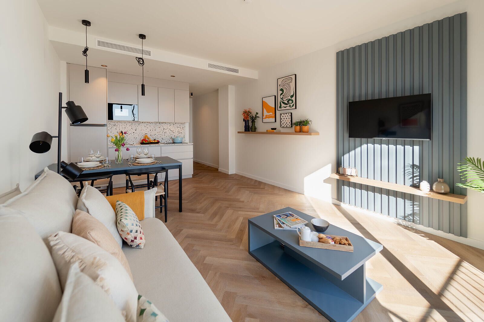A modern living space with a sofa, coffee table, and a dining area with a kitchen in the background.
