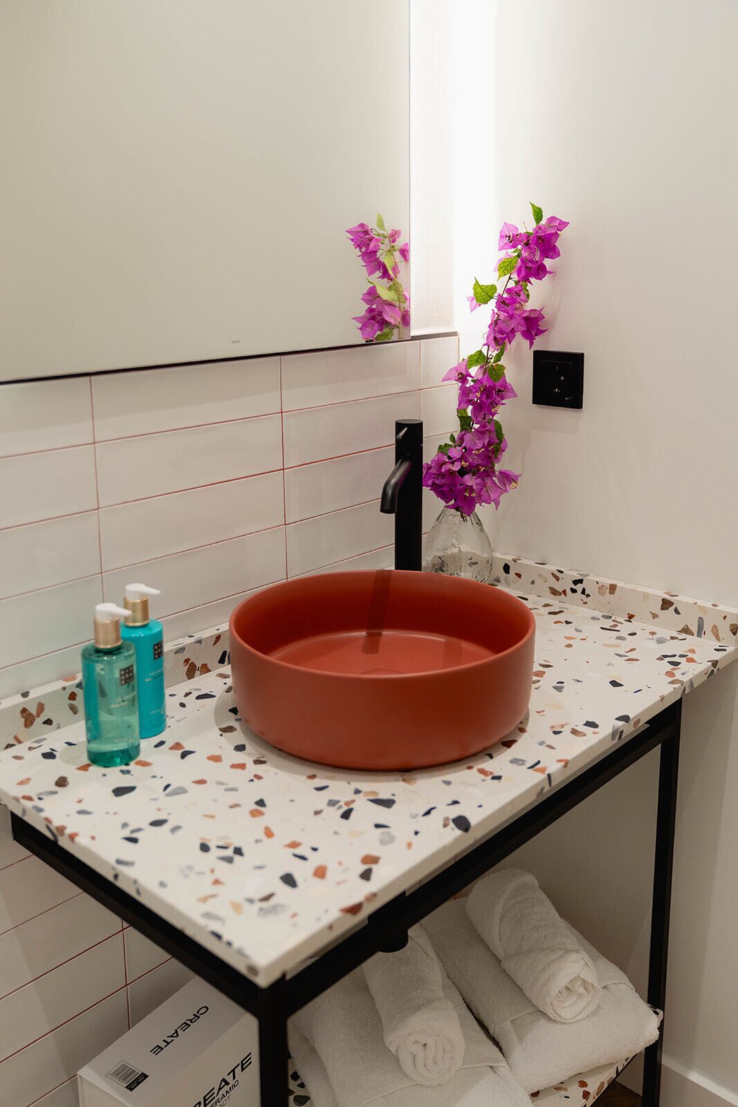 A bathroom with a round sink, a mirror, a towel rack, and a decorative purple plant.