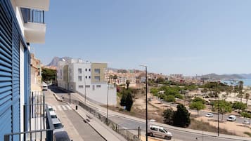Un paisaje urbano costero con edificios modernos, cielo despejado y una carretera con vehículos.